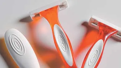 Two orange disposable razors with white grips, close-up on a white background.