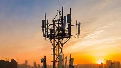Cell phone tower silhouetted against a vibrant sunset over a city skyline.
