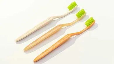Three wooden toothbrushes with bright green bristles, arranged diagonally on a white surface.