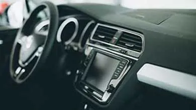Close-up of a modern dark car interior featuring a central touchscreen flanked by chrome-accented air vents.