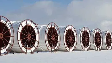 Several large industrial spools wrapped in white tubing sit on snow beneath a cloudy sky.