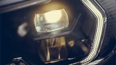 Close-up of a lit modern car headlight emitting a warm light.
