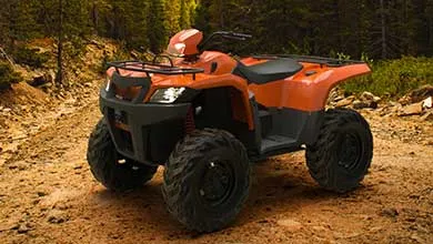 An orange and black all-terrain vehicle parked on a dirt trail in a forest.