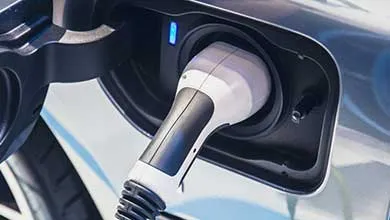 Close-up of a black and white charger plugged into an electric vehicle, with a blue light showing it is charging.