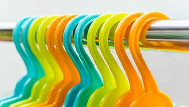 Colorful plastic hangers in turquoise, lime green, and orange hang from a silver metal rod, with their curved hooks visible in the foreground.