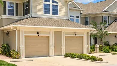 Row of modern residential townhomes with garages, landscaped greenery, and a blue sky overhead.