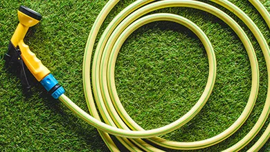 A yellow garden hose with a spray nozzle is coiled on green grass.