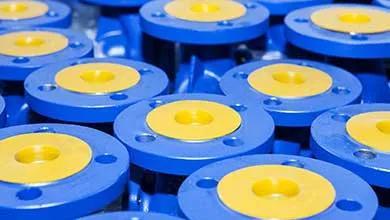 Rows of blue industrial flanges with yellow circular centers, each having bolt holes around the edges.