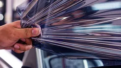 A close-up of a hand peeling back a sheet of glossy, transparent plastic film with visible light reflections.