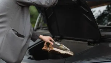 A person in a grey jacket places sneakers into the open trunk of a black car.